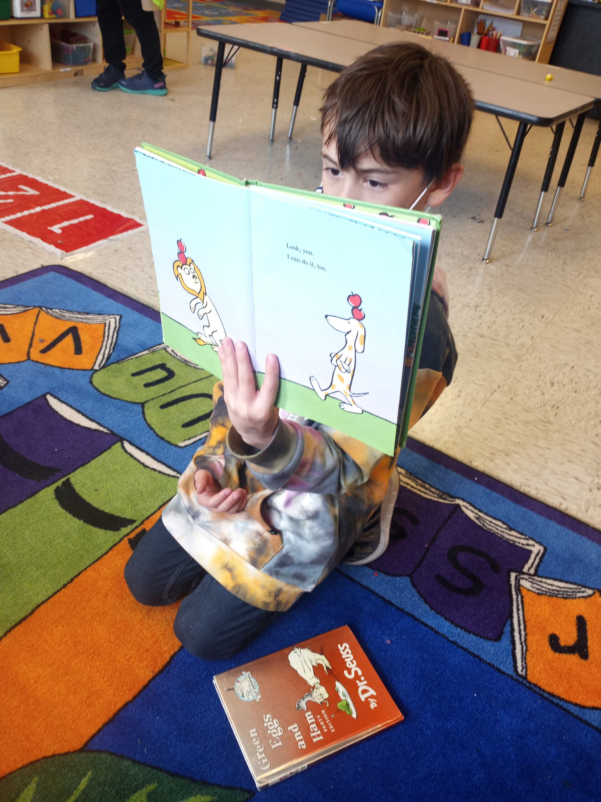 A child sharing a story book on the classroom rug